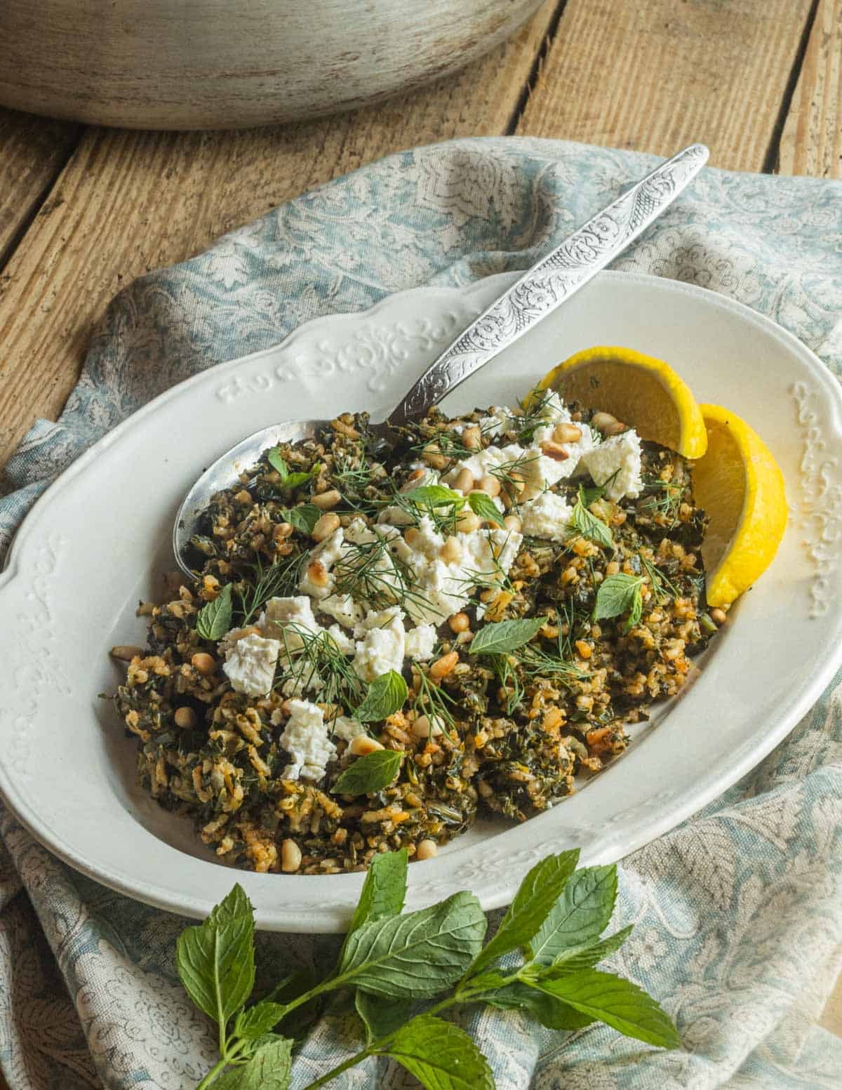 A plate of Greek Spinach Rice or Spanikorizo on a oval china plate garnished with feta cheese, pine nuts, dill and mint.