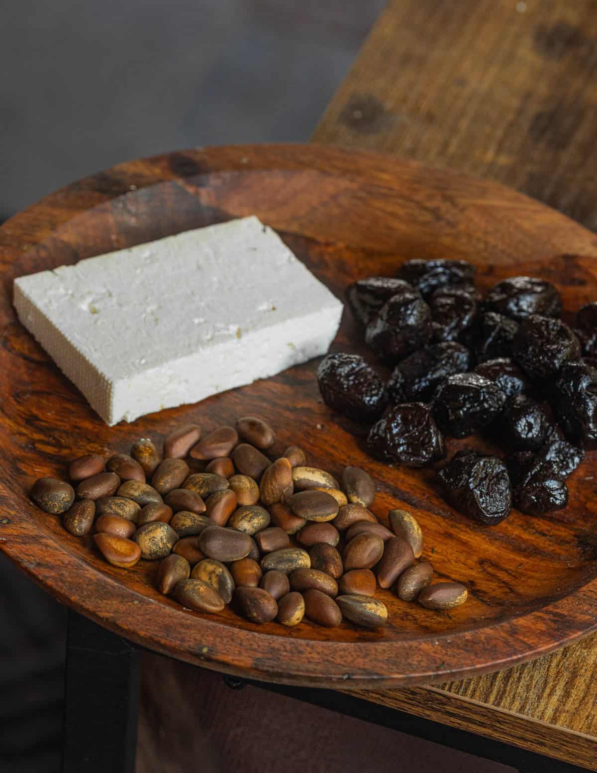 A wooden plate with black olives, wild pine nuts, and feta cheese that could be added to spanikorizzo.