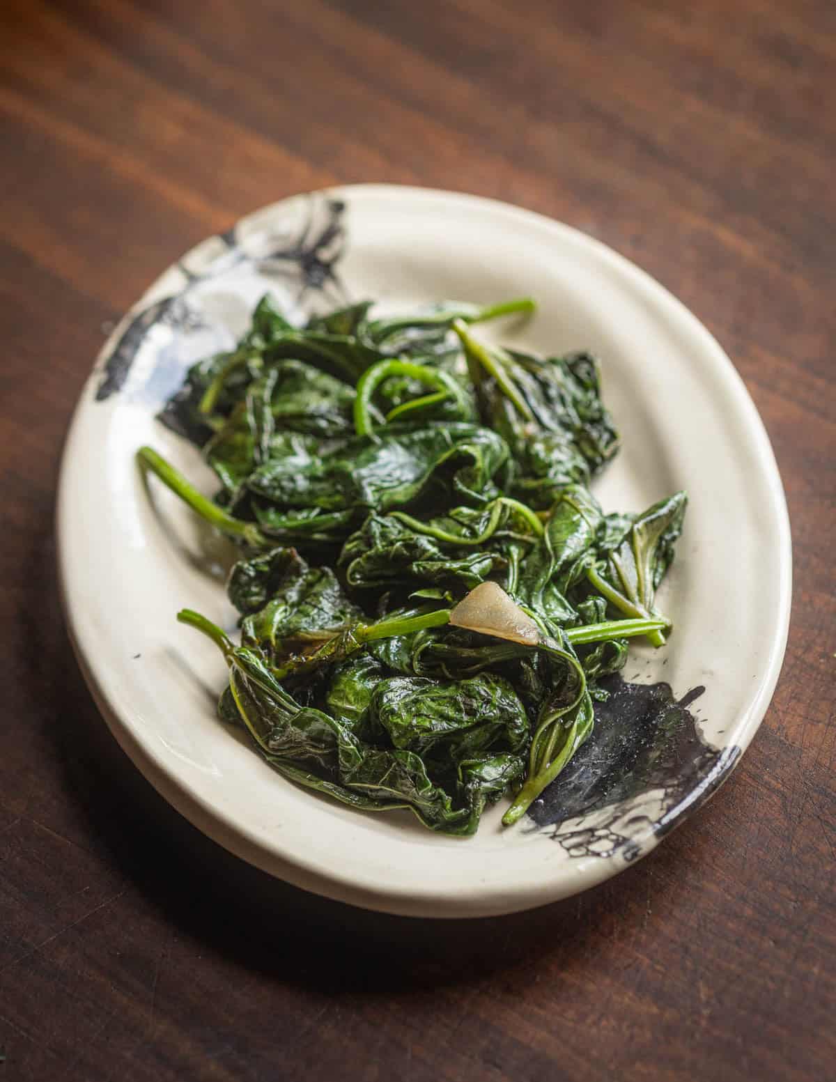 Stir-fried sweet potato leaves with garlic on a small ceramic plate