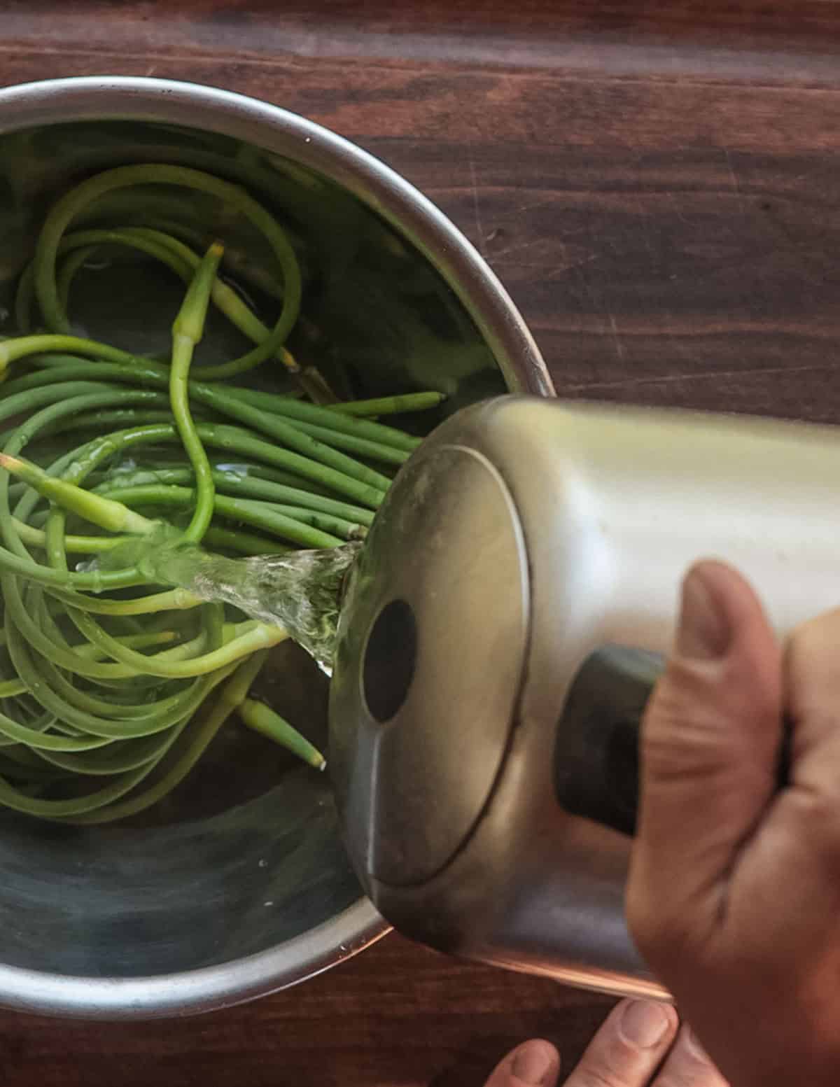 Pouring boiling water over garlic scapes in a bowl to make them easier to cut.