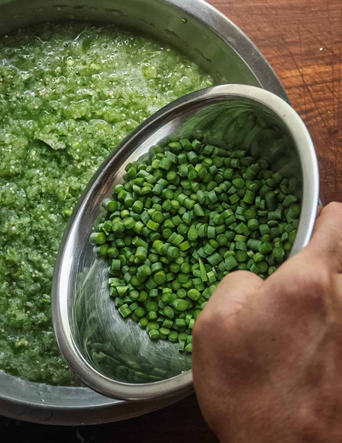 Adding thinly sliced garlic scapes to a bowl of salsa after pureeing.