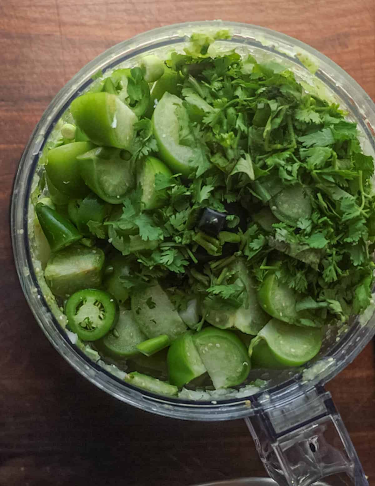 Tomatillo and garlic scape salsa ingredients in a food processor ready to puree.