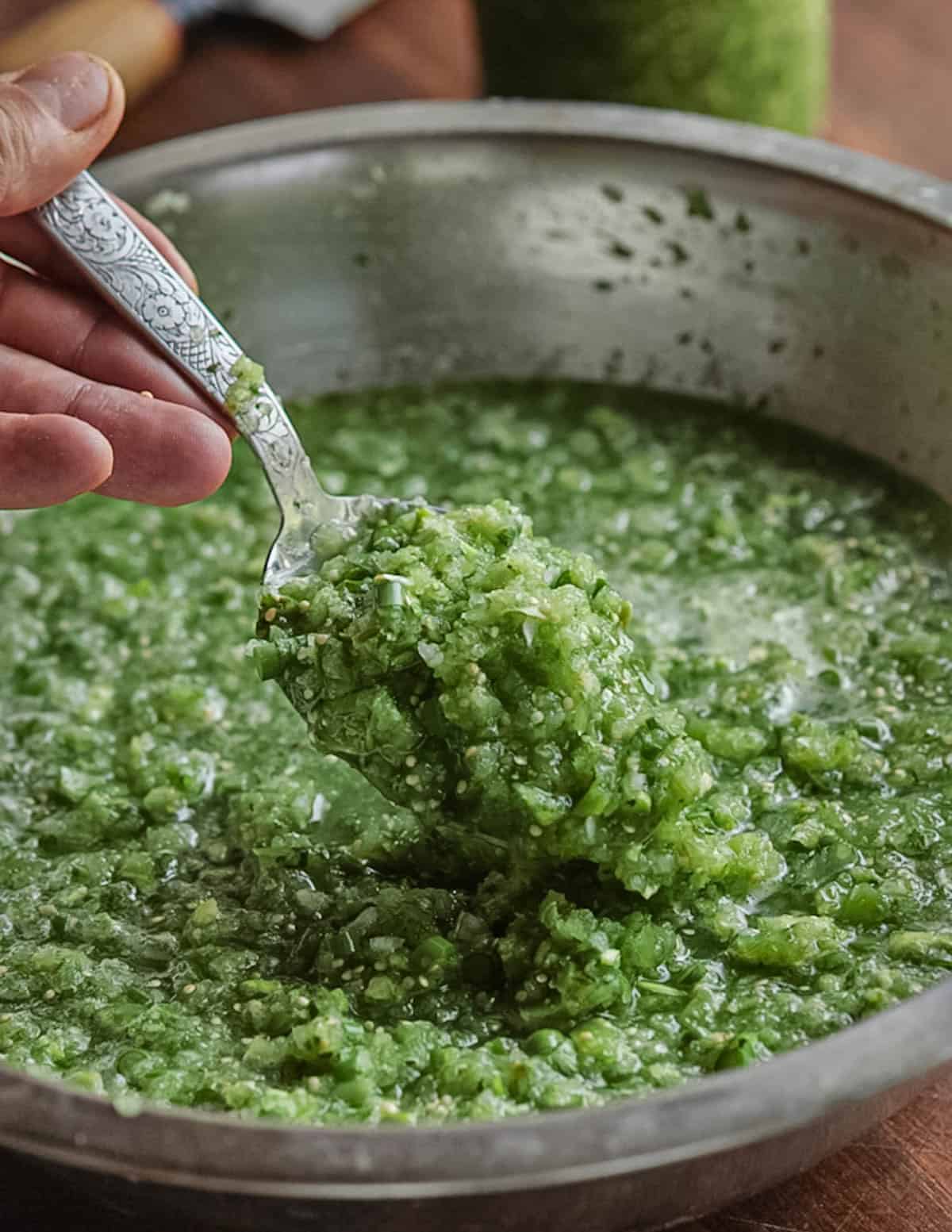 A spoon lifting up garlic scape salsa in a bowl showing the texture of the finished product.