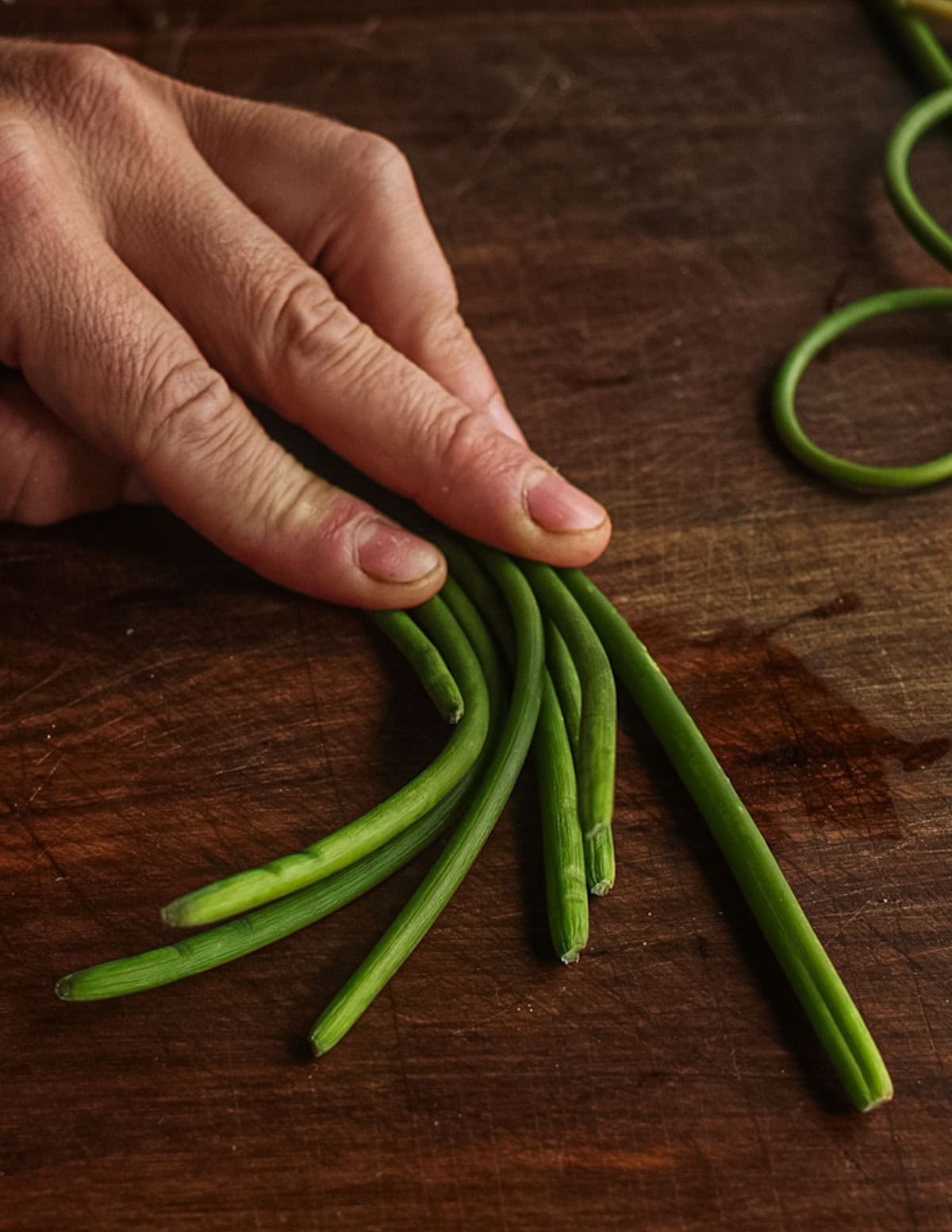 Lining up garlic scapes on a cutting board so they can be easily sliced.