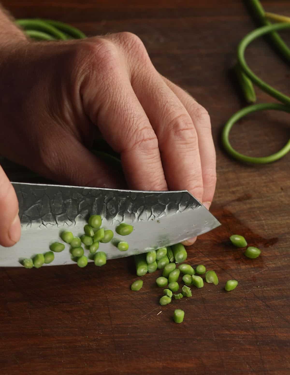 Thinly slicing garlic scapes on a cutting board.