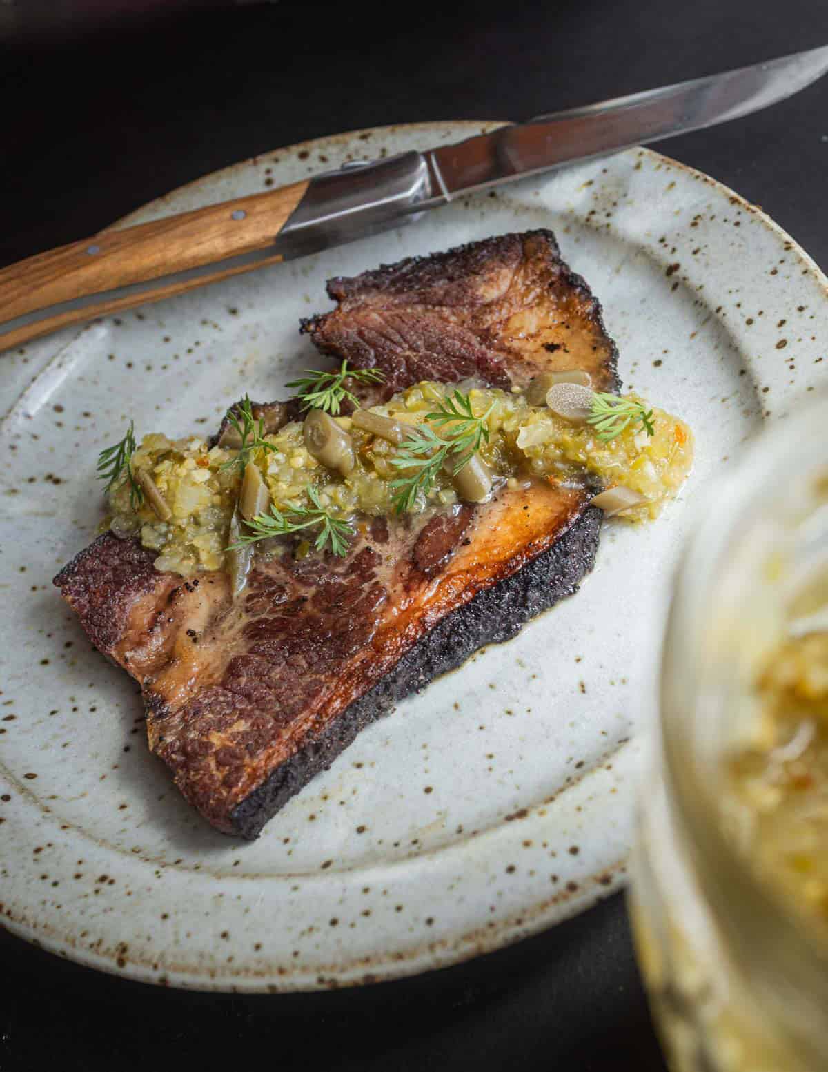 A slice of sauteed beef brisket topped with a spoonful of fresh garlic scape salsa.