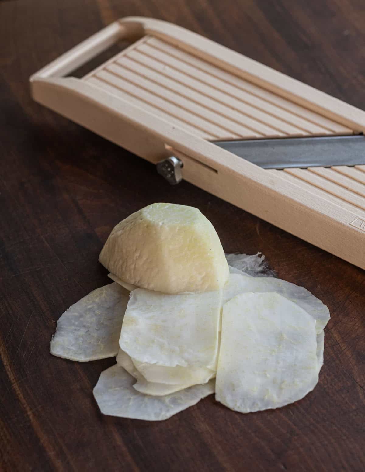 Shaving a peeled kohlrabi bulb on a mandoline slicer.
