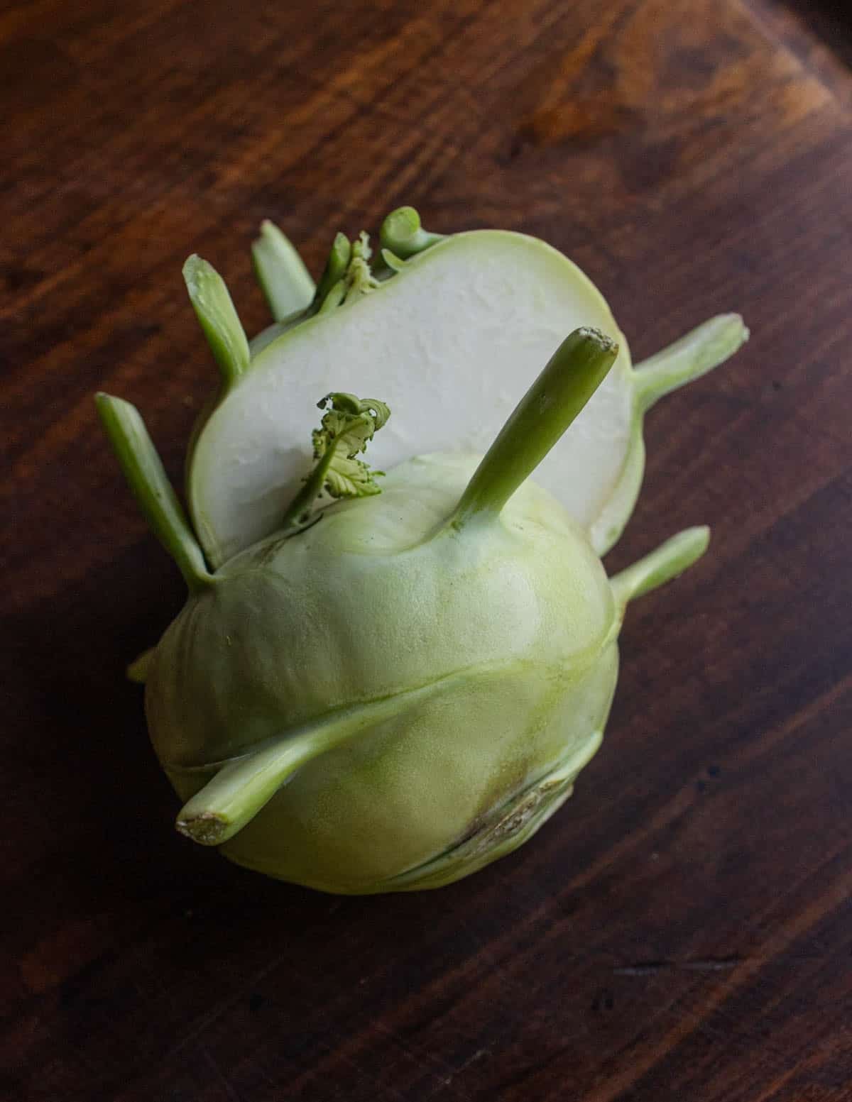 A halved bulb of kohlrabi showing the white inside on a black walnut cutting board.