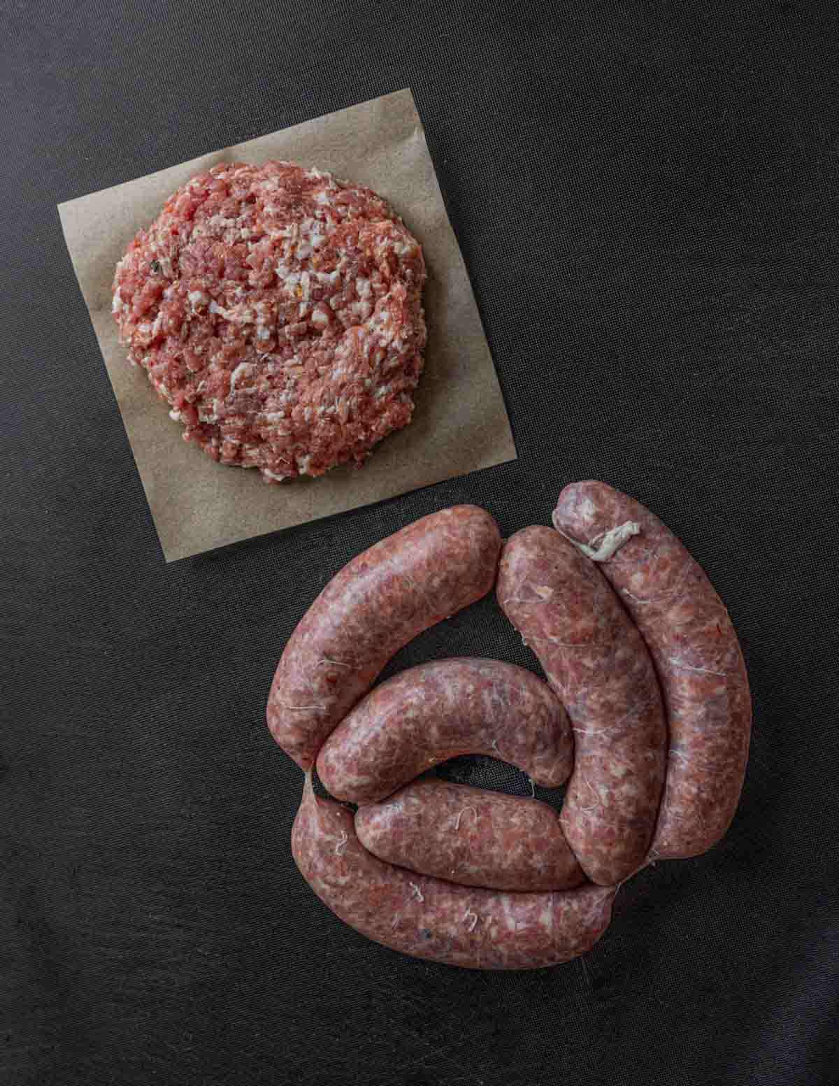 Loose fennel sausage on a piece of parchment next to links of hot Italian fennel sausage.