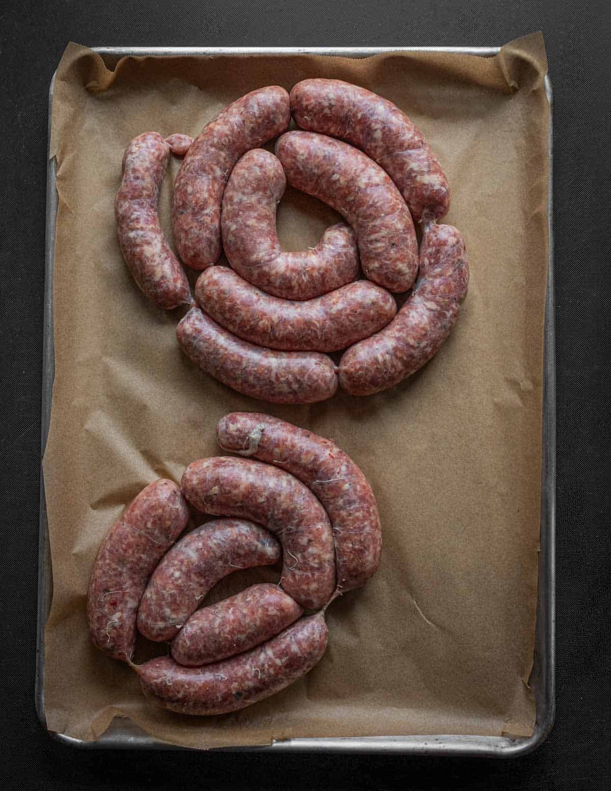 Coils of hot Italian sausage on a baking sheet lined with parchment.
