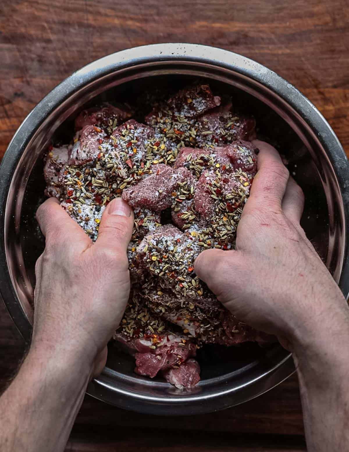 Hands mixing meat with spices in a bowl to make sausage.