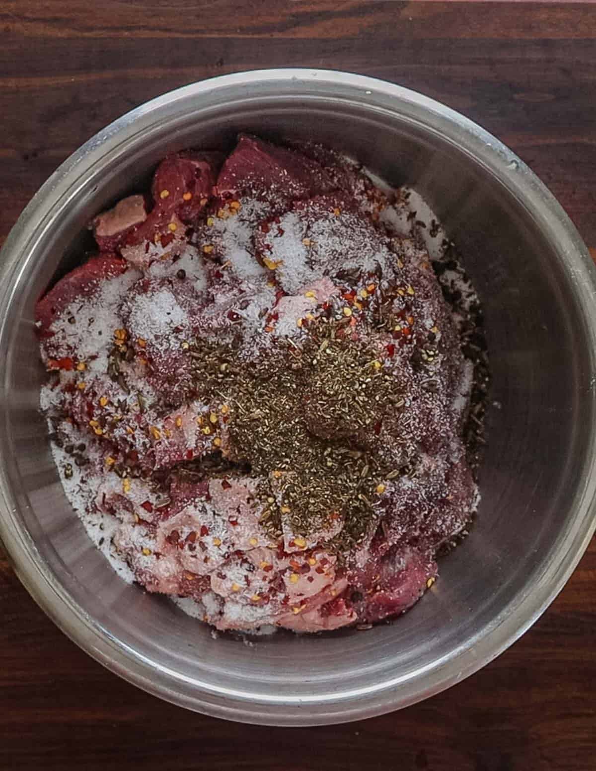 A bowl of diced pork shoulder with black pepper, fennel seed, and red pepper flakes.