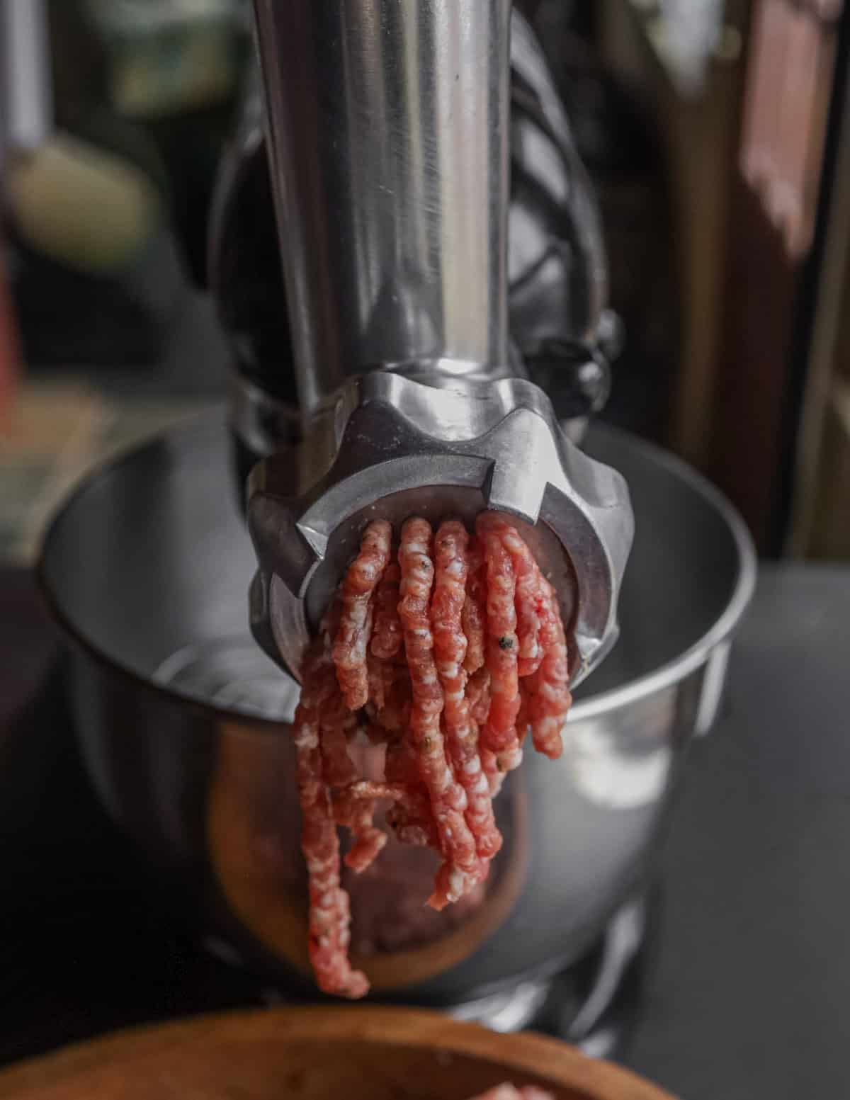 A Kitchen Aid mixer with a meat grinder attachment grinding meat.