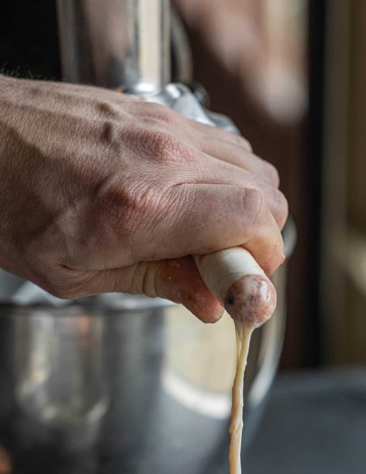 A hand holding sausage casings on a stuffing attachment while the casing fills with sausage.