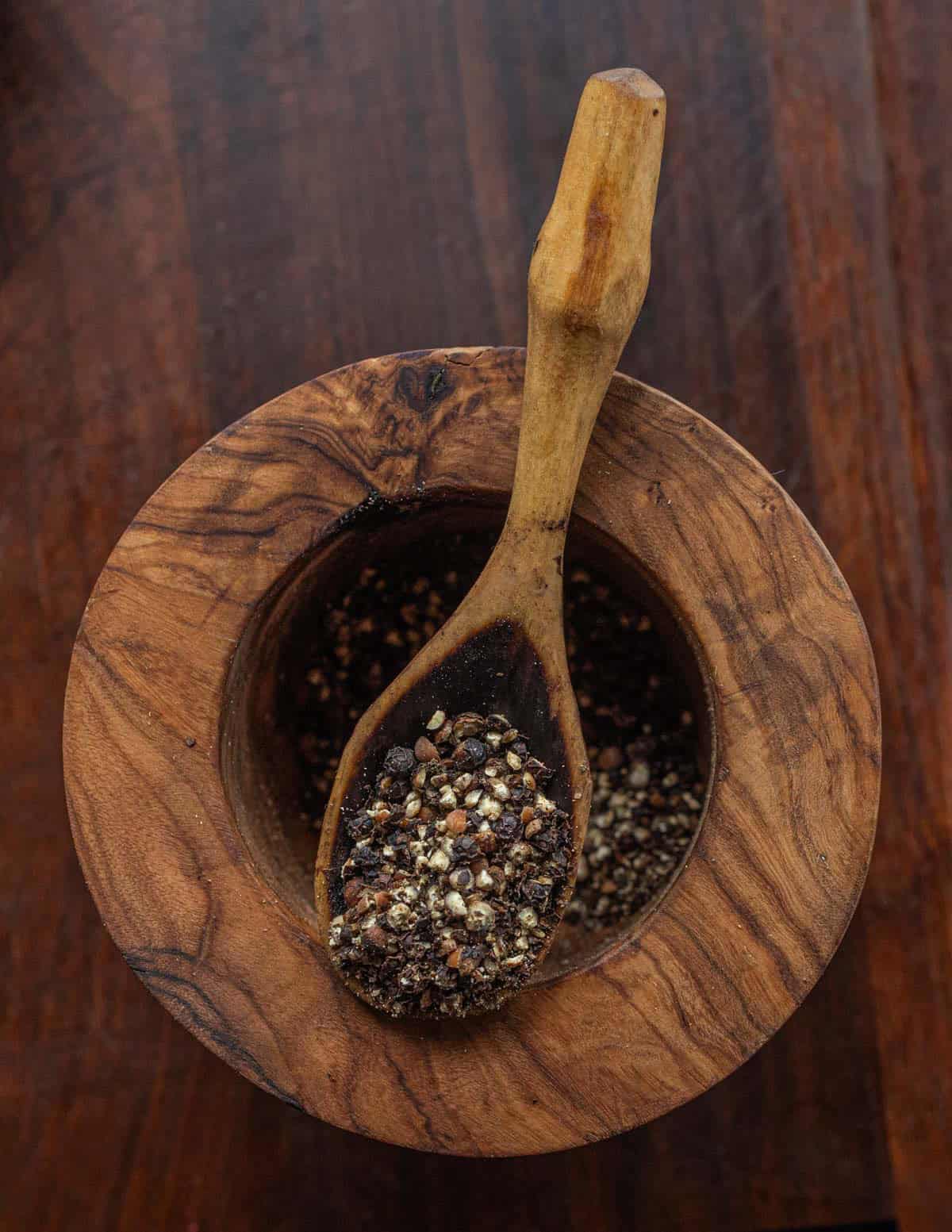 A mortar and pestle filled with crushed black peppercorns to be added to fennel sausage.