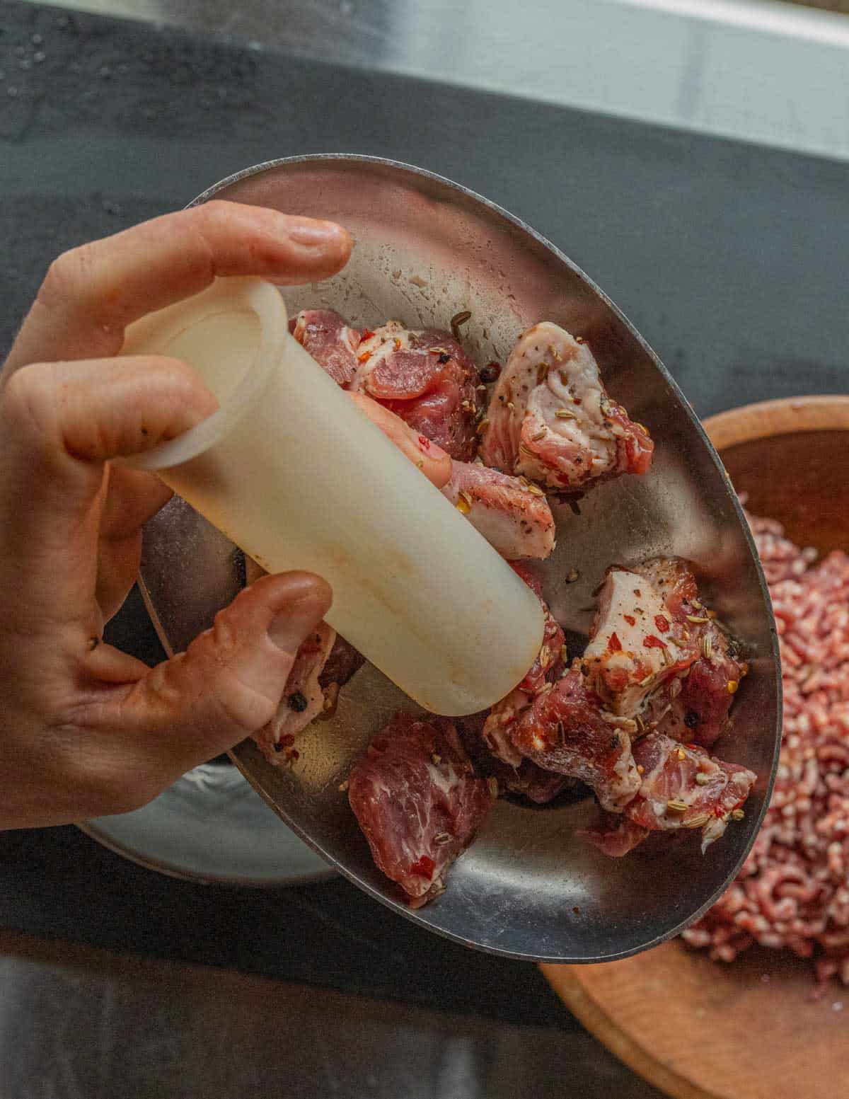 A hand pushing seasoned pork through a meat grinder.