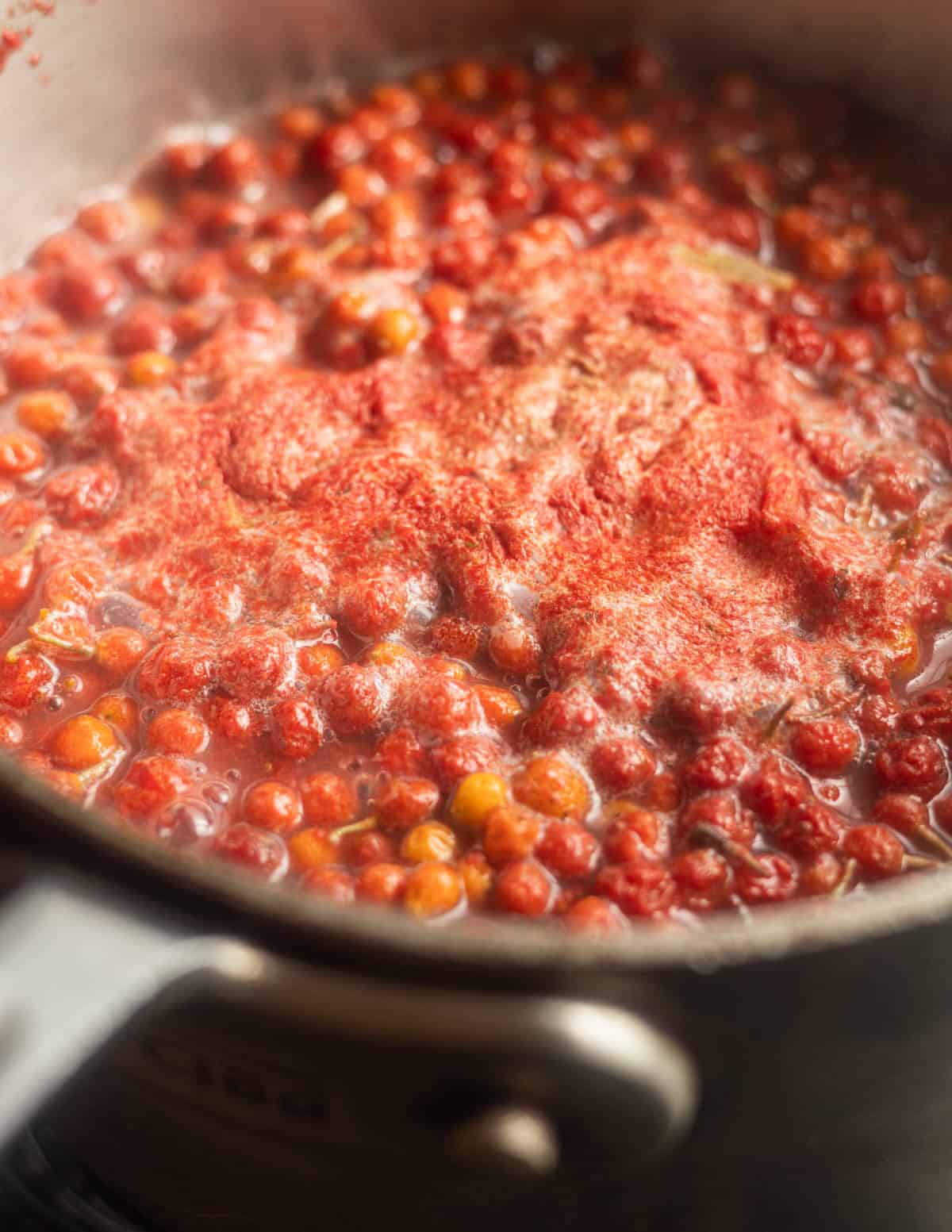 Autumn olive fruit boiled in a pot showing a foamy layer on top and broken up berries.