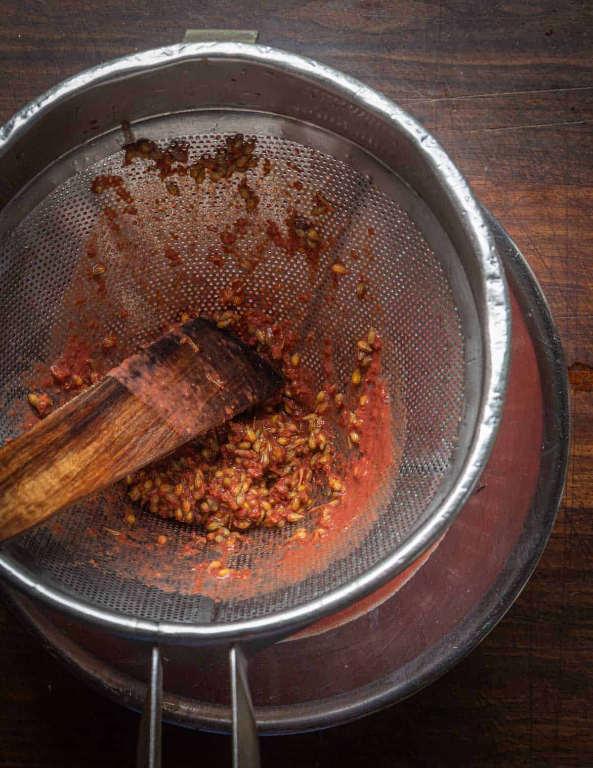 A spatula pressing autumn olive berry puree through a china cap sieve.
