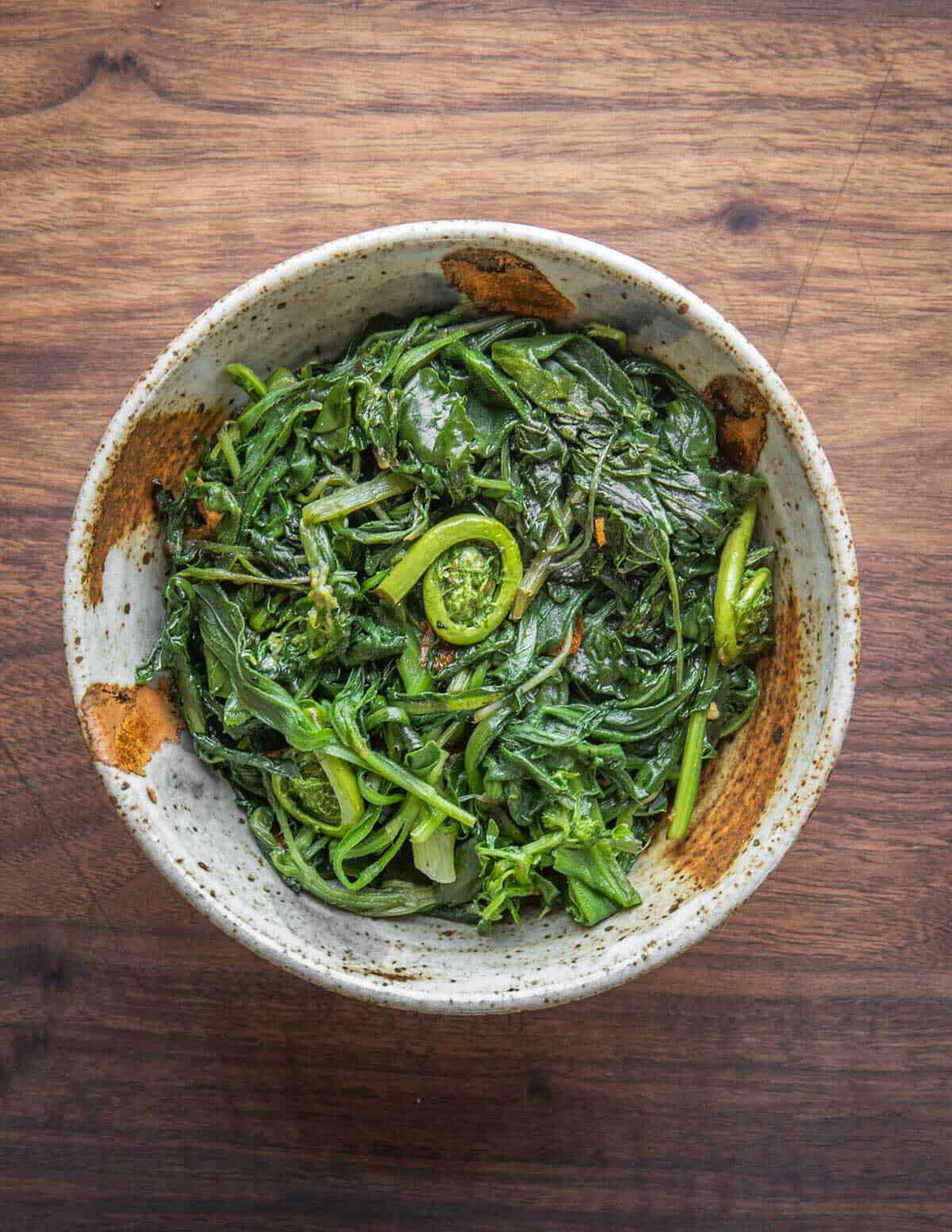 A bowl of cooked borage greens with fiddleheads and other spring leafy greens.
