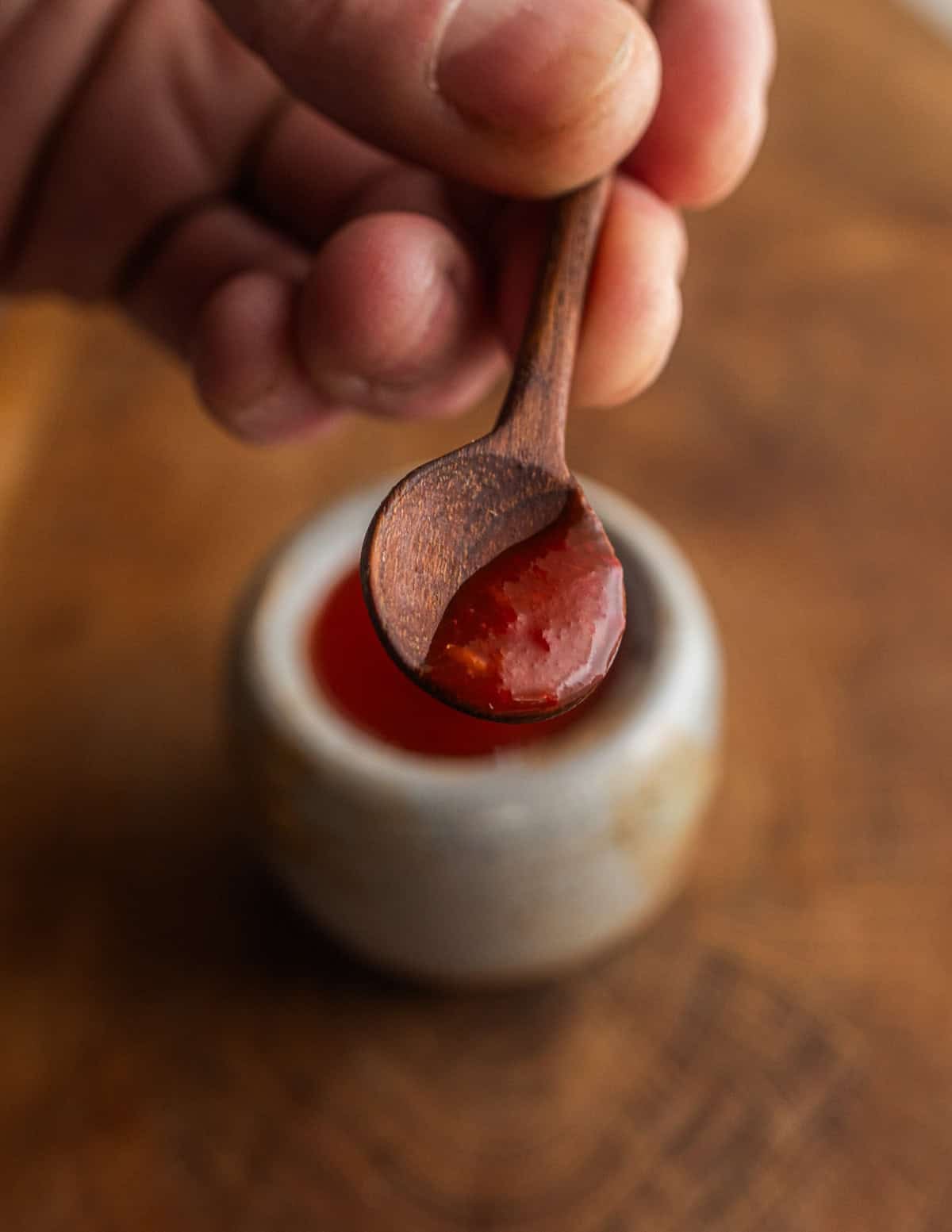 A hand holding a small wooden spoon filled with a small amount of fermented maple hot sauce.
