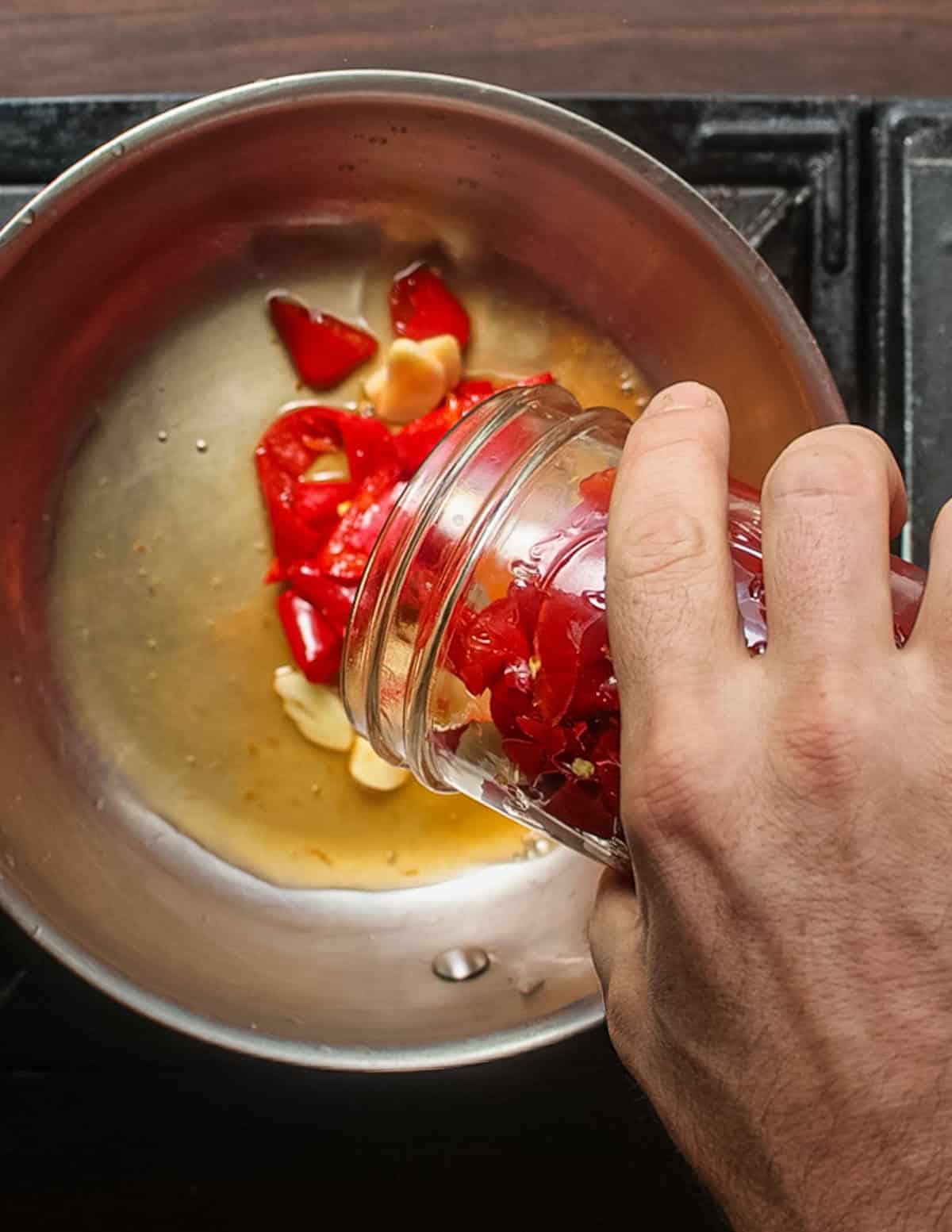 Emptying a jar of fermented peppers and garlic into a pot to cook and make hot sauce.