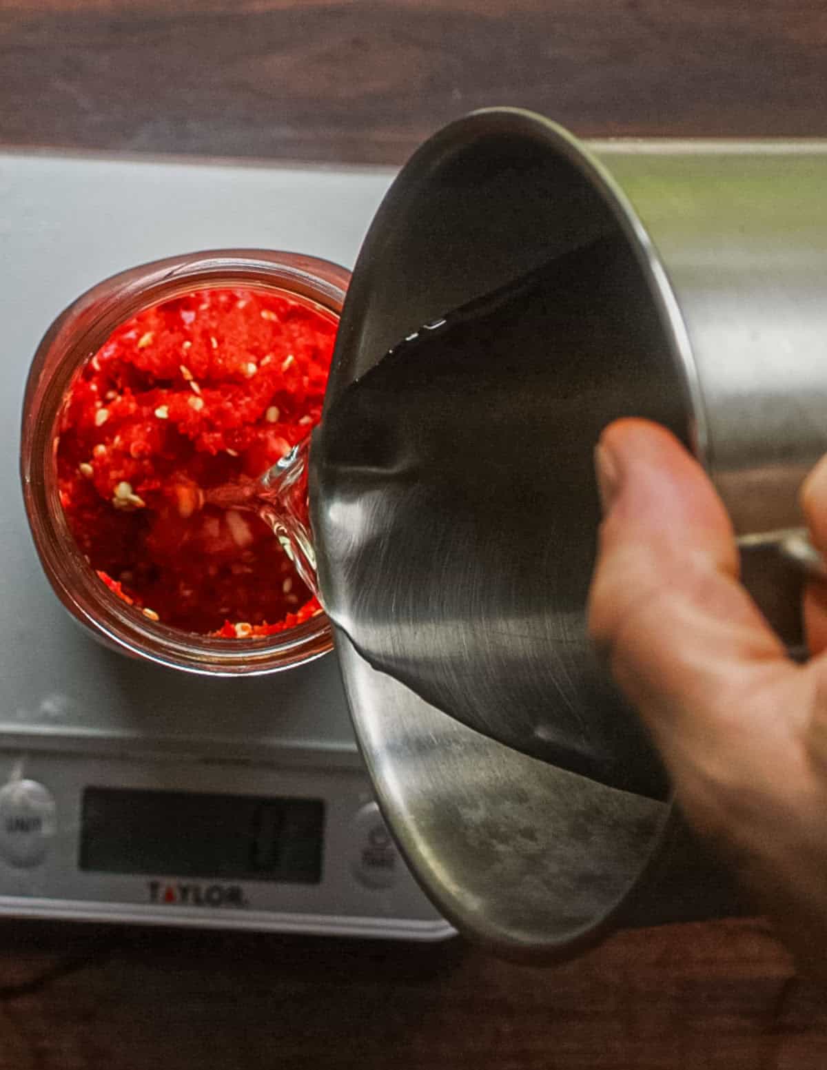 Adding water to a jar of ground fresno chilis on a scale.