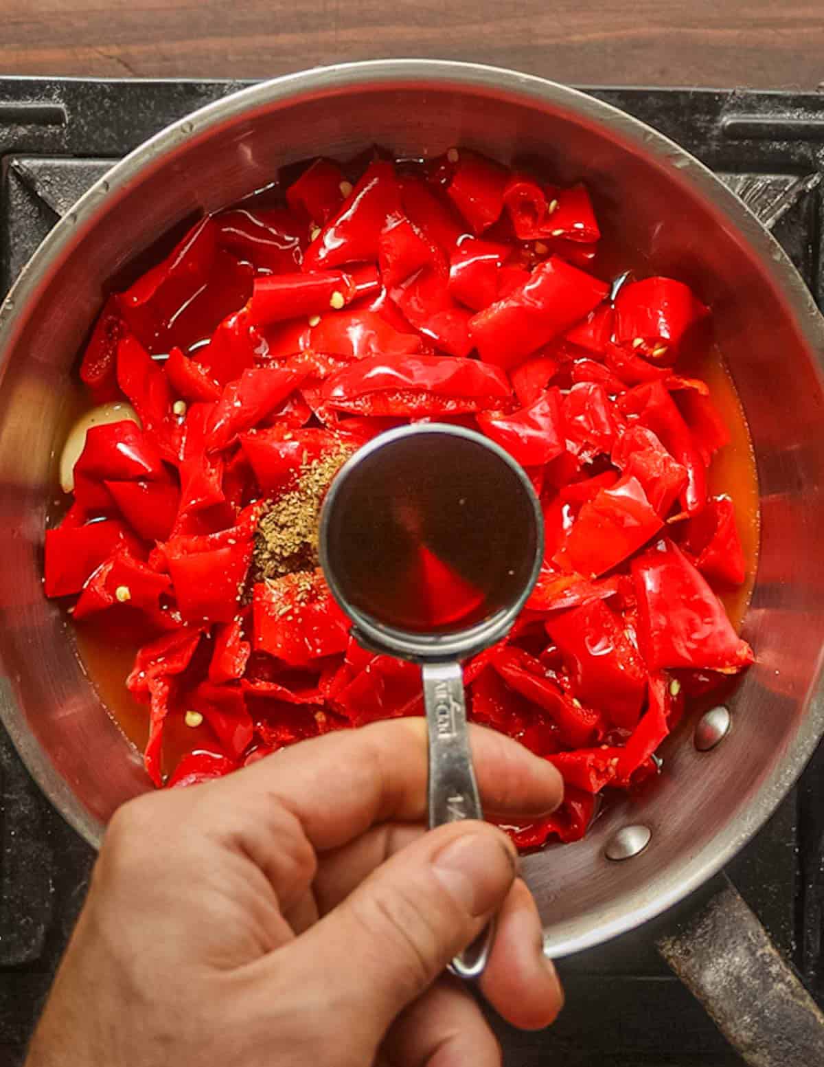 Adding maple syrup to a pan of fermented peppers cooking for hot sauce.