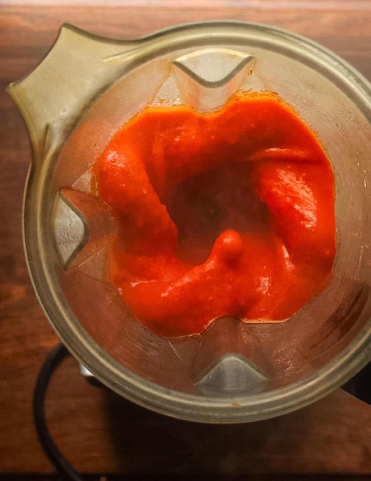 A top-down image showing fermented red fresno hot sauce being pureed in a vita mix blender.