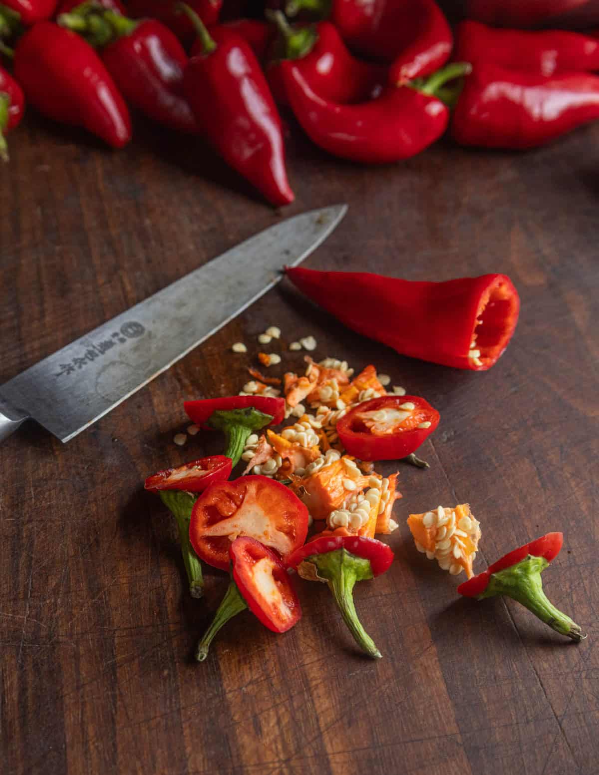 A knife on a cutting board showing red Fresno peppers being de-stemmed and seeded before fermenting into hot sauce.