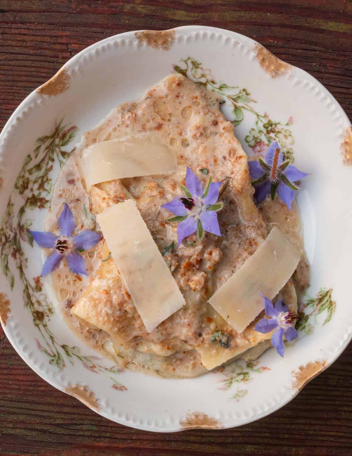 A bowl of Ligurian pansotti with walnut sauce garnished with borage flowers.
