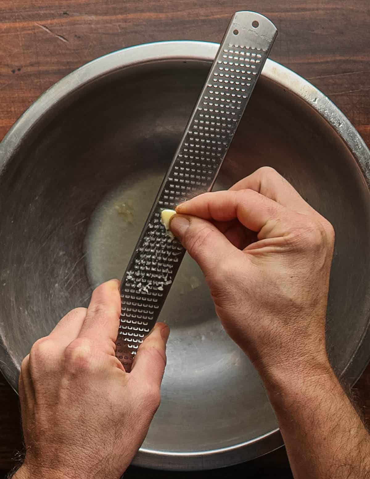 Grating garlic into a mixing bowl with lemon juice.