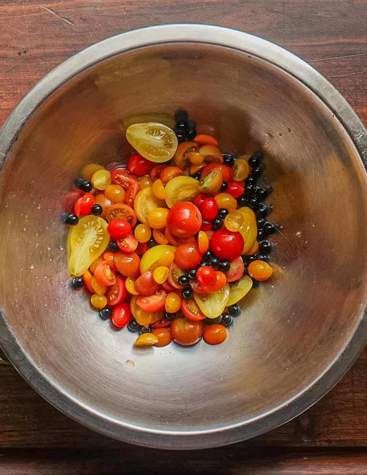 A mixing bowl with grated garlic and lemon juice with fresh cherry tomatoes added.