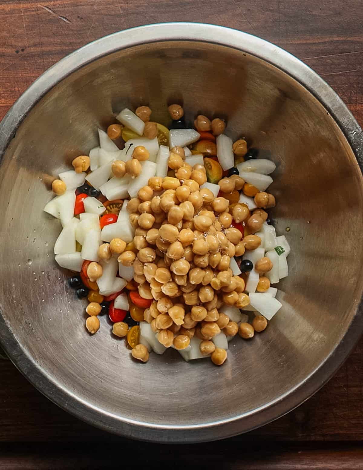 Adding chickpeas to a salad of tomatoes and cucumbers in a bowl.