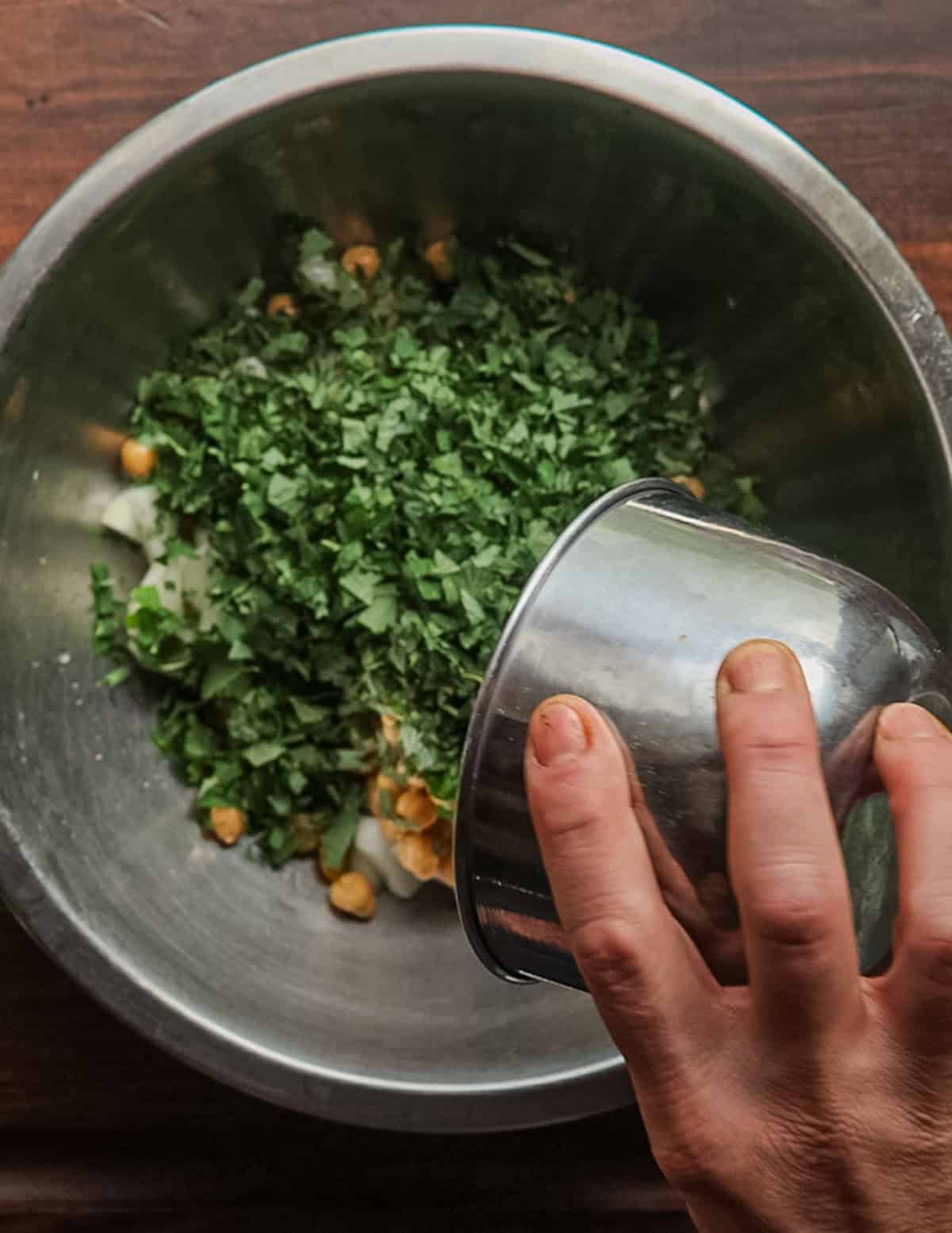 Adding finely chopped salad burnet leaves to a bowl of chickpeas, tomatoes and cucumbers.