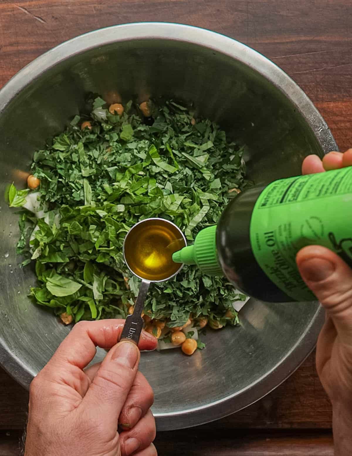 Adding extra virgin olive oil from a squeeze bottle into a vegetable salad in a bowl.