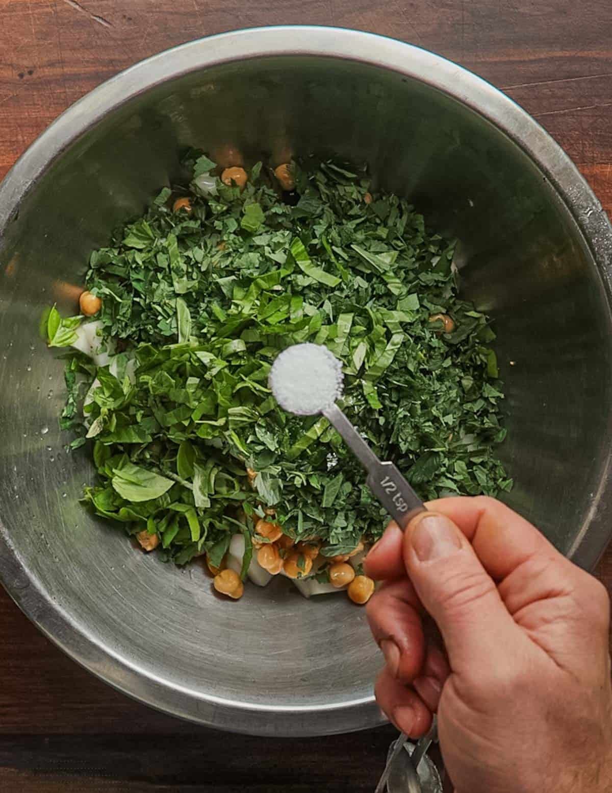 Adding salt to a fresh vegetable salad in a bowl.