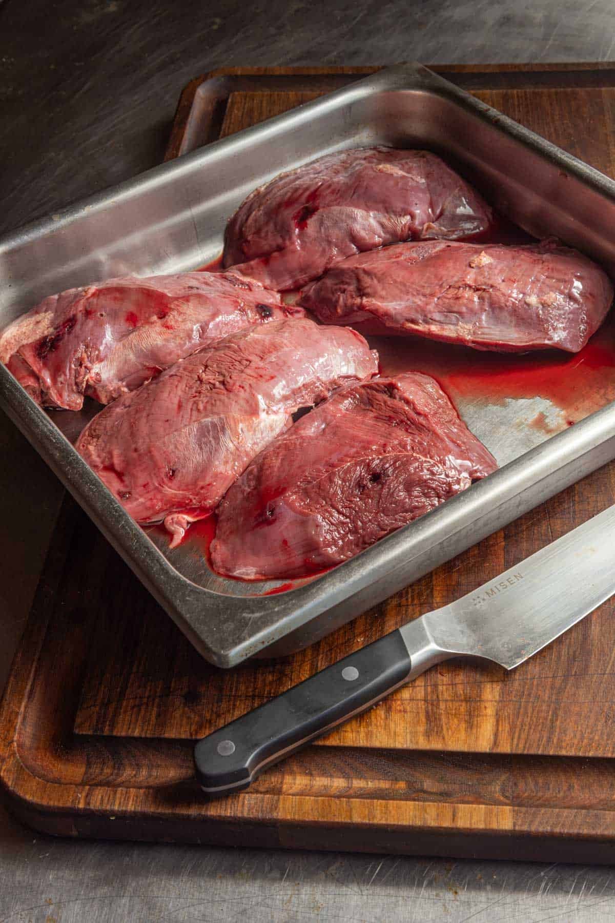 A wide stainless steel pan filled with trimmed Canada goose breasts ready to cook.