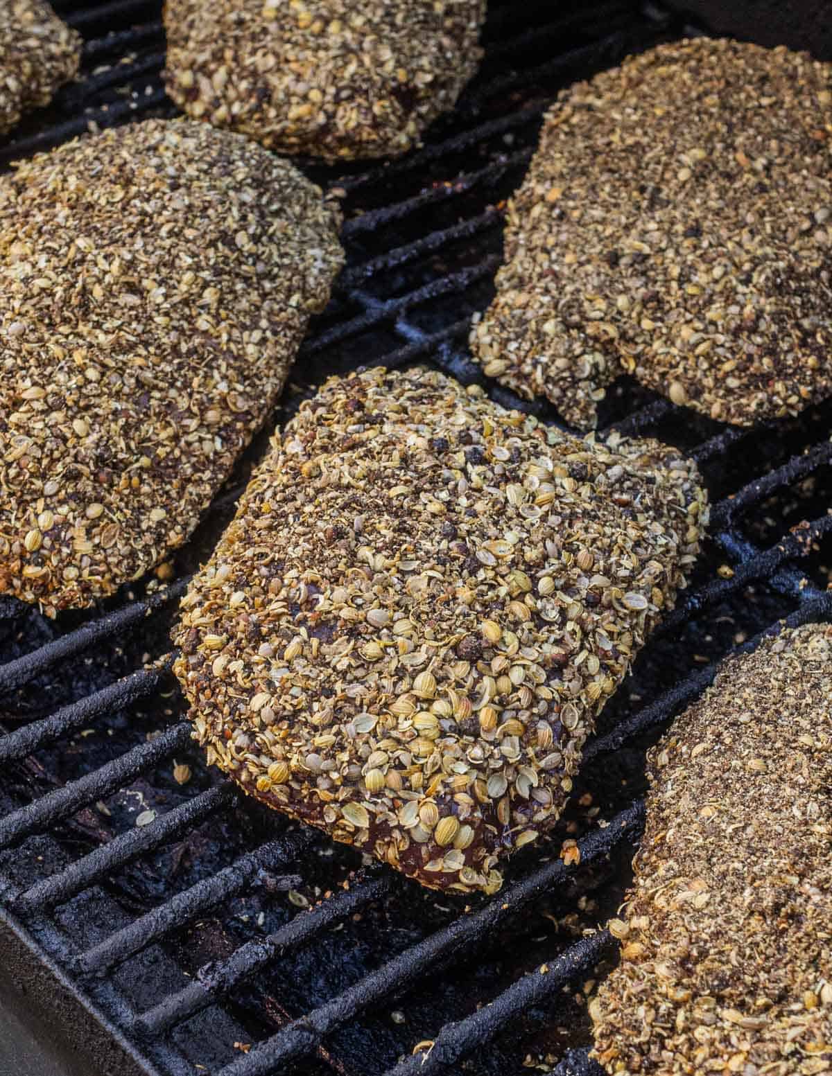 Many goose pastrami breasts crusted with coriander and peppercorns smoking on a pellet smoker.