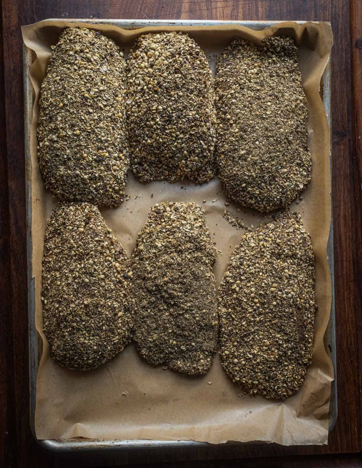 Six cured Canada goose breasts on a baking sheet crusted with peppercorns and coriander and ready for the smoker.