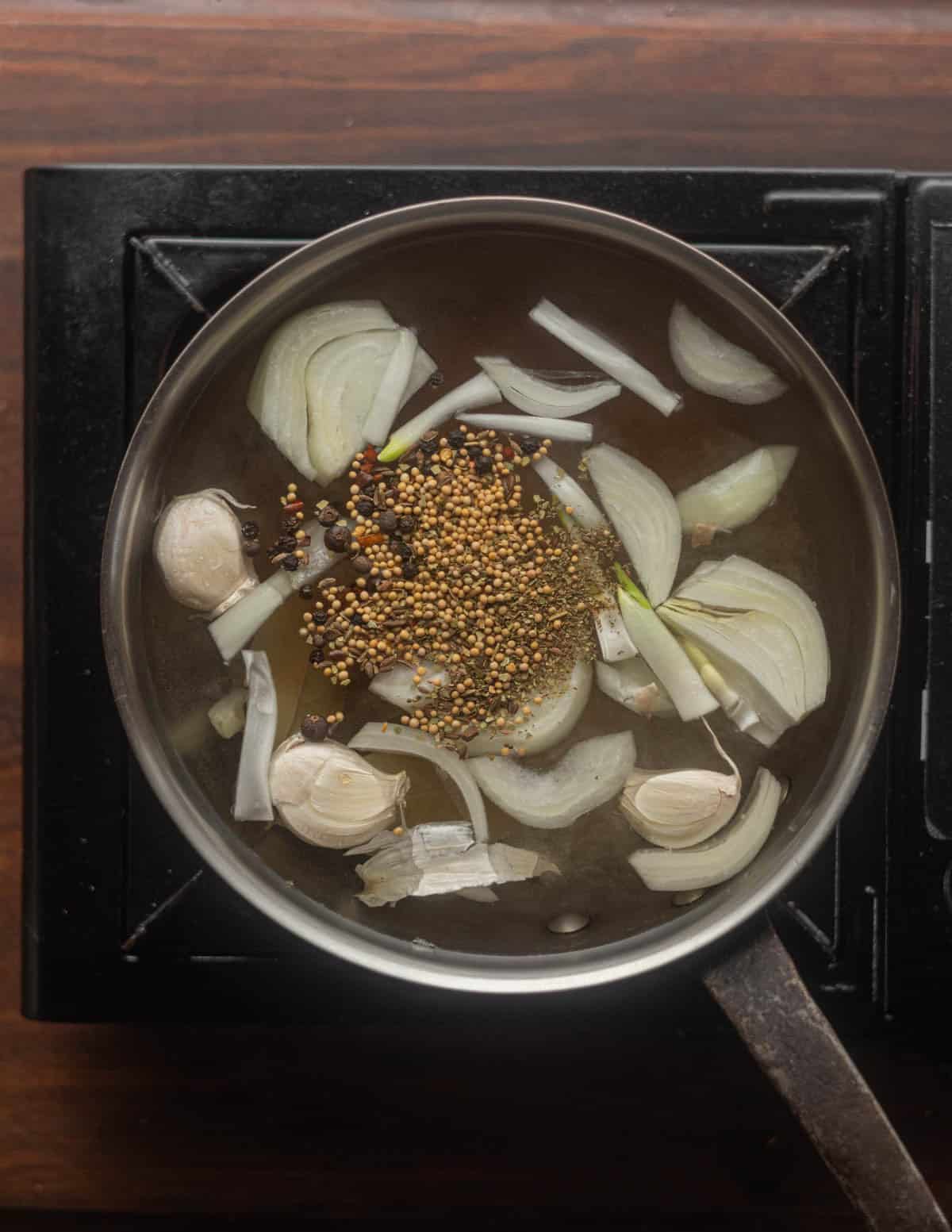 Cooking a pastrami brine for goose breasts with onion, pickling spices, bay and garlic in a pot.