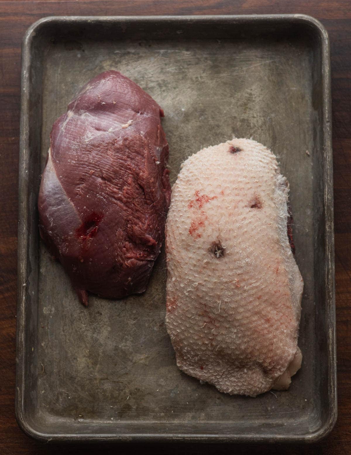 Two Canada goose breasts side by side. One skinless, one plucked showing holes from shot that entered the breast.