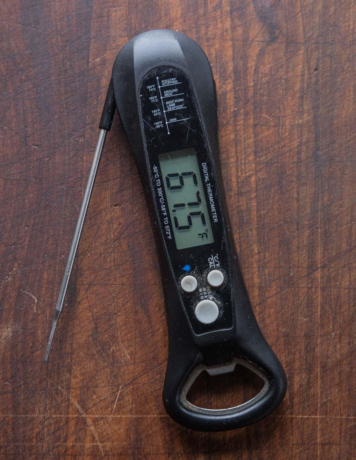 A close up image of an instant read thermometer on a black walnut wood background.