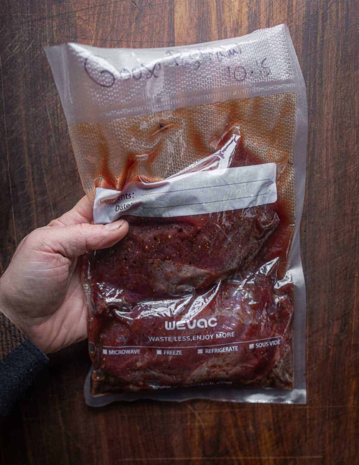 A hand holding a bag of vacuum sealed goose pastrami showing the brine formed naturally in the bag.