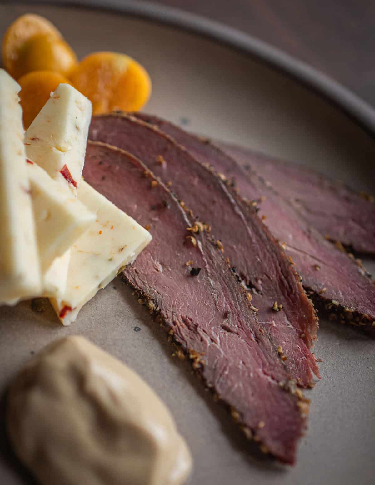 A close up image of thinly sliced goose pastrami with ground cherries, cheese and mustard on an appetizer plate.
