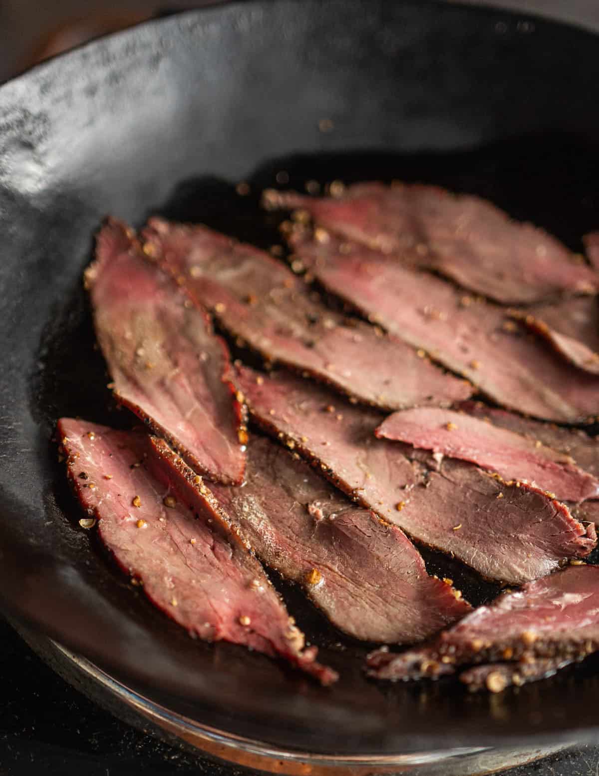 Thinly sliced goose pastrami cooking in a Kehoe carbon steel pan.