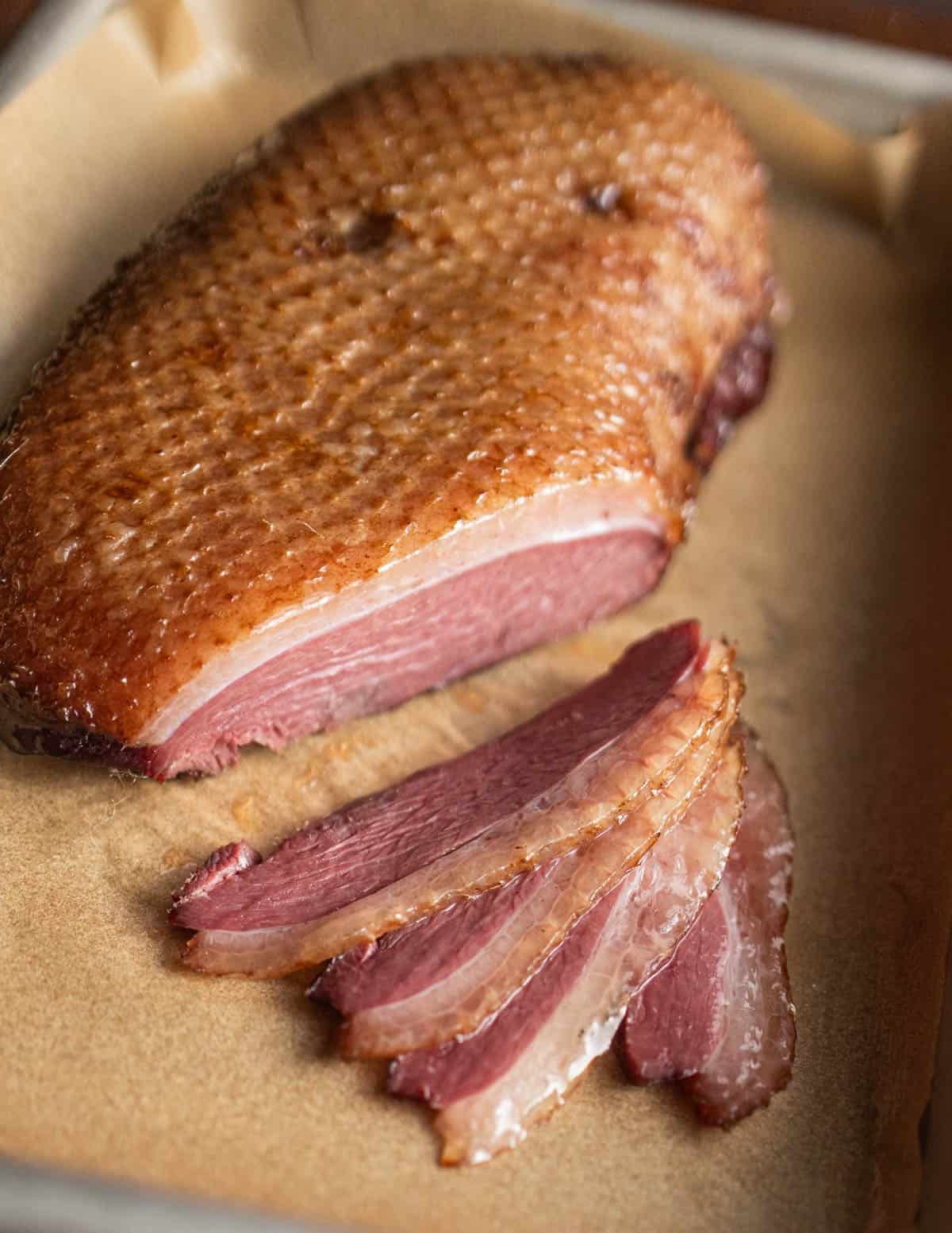 A smoked skin-on Canadian goose breast sliced on a baking sheet.