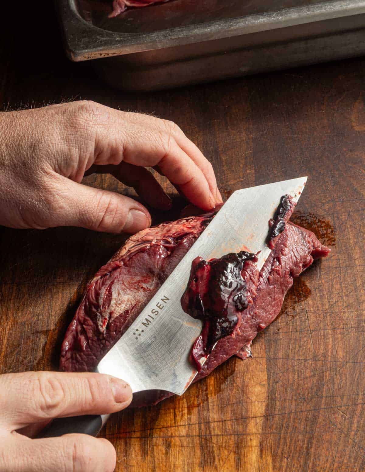 Using a knife to cut off coagulated blood from a goose breast.