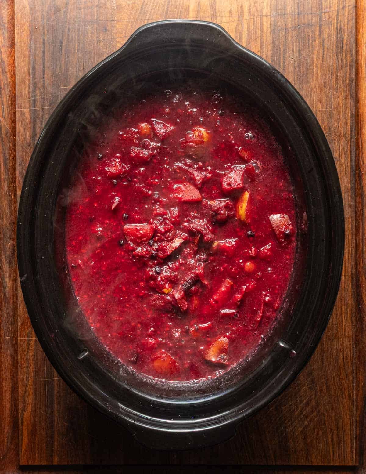A top down image of a slow-cooker filled with a variety of cooked fruit that's soft and released it's juice.
