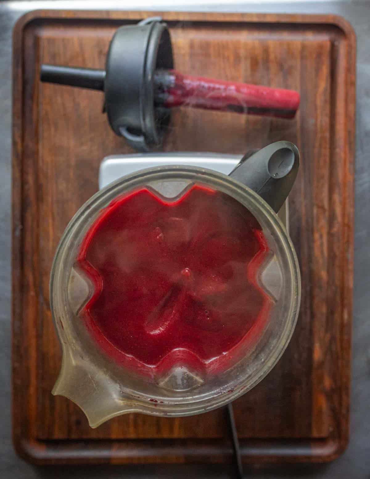 A Vitamix blender filled with apple, cranberries, blueberries and strawberries.