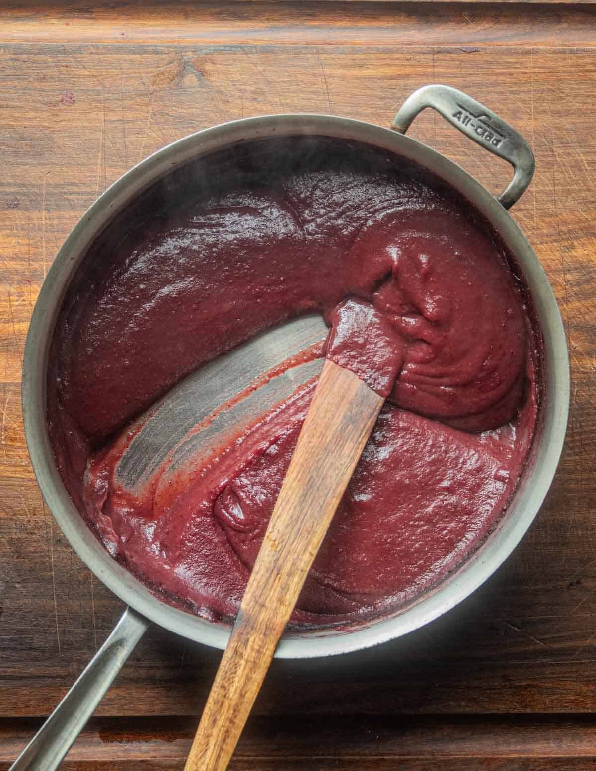 A wide all clad pan filled with purple fruit puree after baking to remove water before dehydrating.